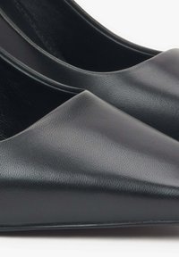 Czarne płaskie buty z faux skóry o ostrym nosku, o gładkiej fakturze i minimalistycznym designie. Subtelne przeszycia wzdłuż brzegów, bez widocznych elementów metalowych.