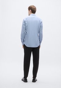 Heleroheline pika varrukaga särk nööpidega kraega, sirge lõike ja külgsete plekkidega, kombineeritud mustade pükste ja mustade kingadega.