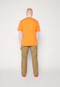 Oranžové bavlněné tričko s krátkými rukávy, kombinované s hnědými cargo kalhotami s bočními kapsami a červenými teniskami.