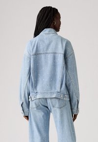 Světle modrá džínsová bunda se zdobnými hroty, oversized design a klasickým límcem. Pěkně střižená v pase s bočními kapsami.