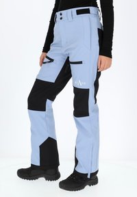 Light blue and black soft-shell pants with zipper pockets and reinforced knee areas. Features a logo on the thigh and a snug fit.