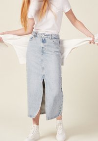 Gonna in denim blu chiaro con spacco frontale, design a vita alta e orlo sfilacciato. Abbinata a una maglietta bianca e scarpe da ginnastica bianche.