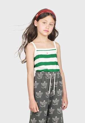 Pige iført en ærmeløs grøn og hvid stribede tanktop med firkantet halsudskæring, parret med grå bukser med logo-print og snoretræk.