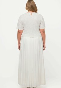 Abito maxi bianco plissettato con corpino texturizzato a maniche corte e dettaglio a oblò sulla schiena. Tessuto morbido con delicate decorazioni.