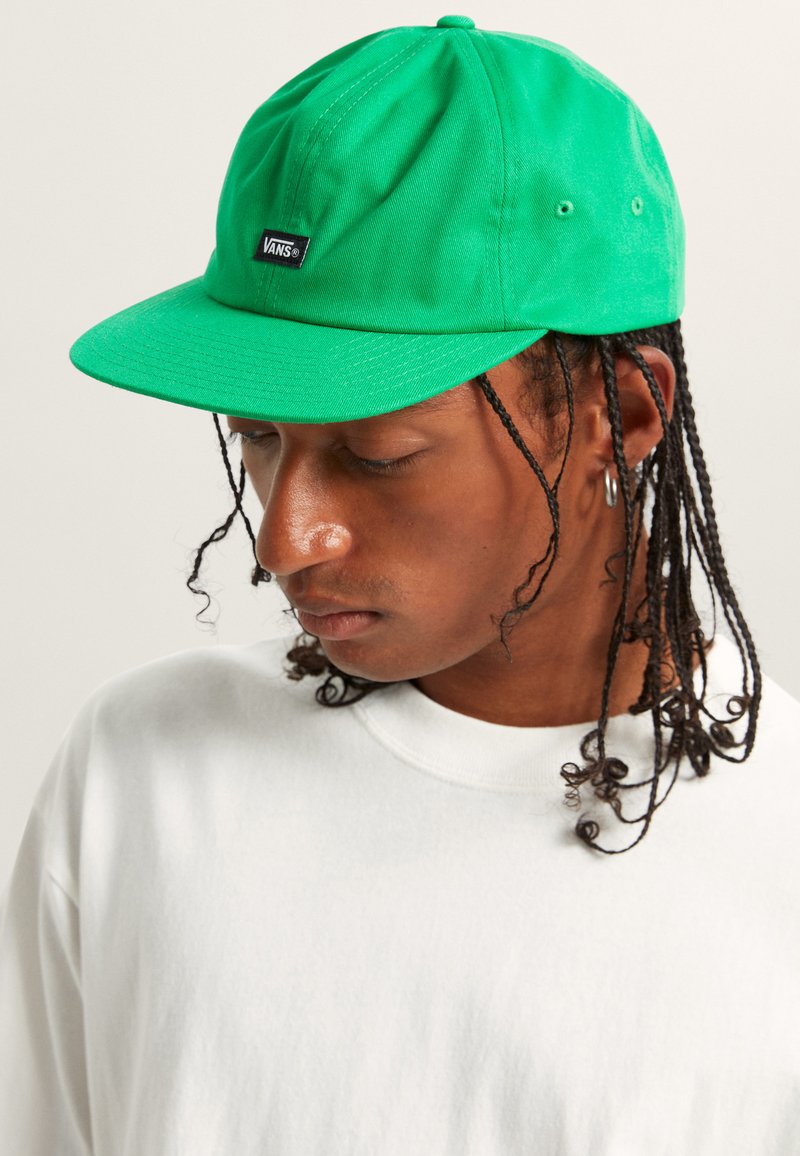 Casquette plate verte en coton avec un patch logo Vans sur le devant. Dispose d'une construction à six panneaux et de trous de ventilation.