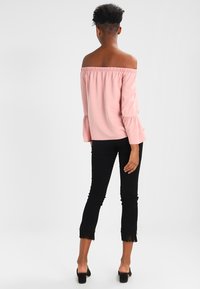 Top rosa chiaro off-shoulder con maniche a volant, abbinato a jeans neri a vita corta con orlo sfrangiato e tacchi alti neri eleganti.