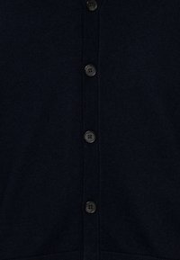 Mörk marinblå stickad tyg med vertikalt placerade svarta knappar sömmade i en enda rad ner i mitten.