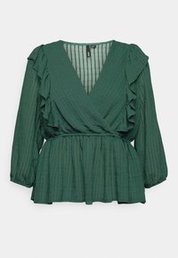 Blouse à manches longues vert foncé avec encolure en V, détails à volants sur le devant et les épaules, taille froncée et rayures verticales texturées.