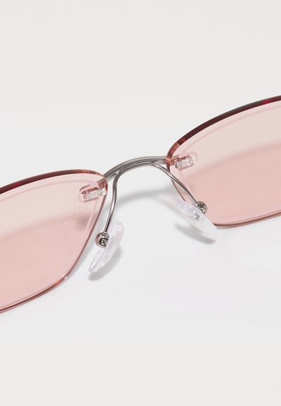 Pink-tinted sunglasses with metal frame, angular lenses, and clear nose pads. Notable for their sleek design and minimalist accents.
