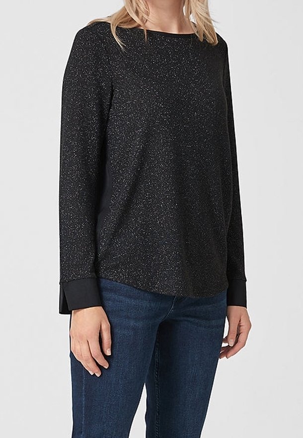 Schwarzes langärmliges Oberteil mit dezenten Glitzerpartikeln, Rundhalsausschnitt und kontrastierenden schwarzen Bündchen. Kombiniert mit blauen Jeans mit einer lockeren Passform.