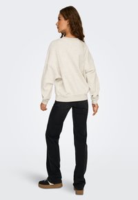 Ljust grå oversized sweatshirt med neddragna axlar, elastisk nederkant, ihopparad med svarta raka byxor och svarta skor med en tan-färgad sula.