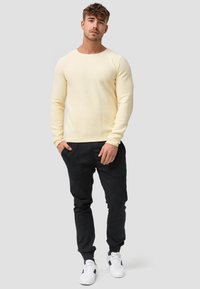 Helles gelbes langärmliges Strickpullover mit rundem Ausschnitt, kombiniert mit schwarzen engen Hosen und schwarz-weißen Sneakers.