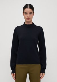Zwarte gebreide trui met een hoge hals, lange mouwen en geribde manchetten. Glad textuur en slim-fit ontwerp, gecombineerd met olijfgroene broek.