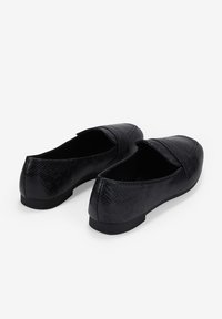Zapatos planos negros con un acabado texturizado de estampado de serpiente, con puntera redondeada y una suela baja negra, que presentan un diseño simple y de fácil puesta.