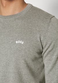 Sweat-shirt gris en coton avec un col rond et des poignets côtelés, arborant un petit logo blanc "BOSS" sur le devant. Texture douce.