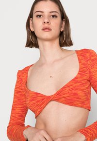 Top cropped em vermelho e laranja com design frontal torcido e mangas longas, feito em tecido texturizado, apresentando um decote largo.