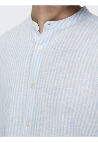 Camicia in lino azzurro chiaro e bianca a righe, con colletto alla cinese, dotata di chiusura con bottoni e un tessuto testurizzato e traspirante.