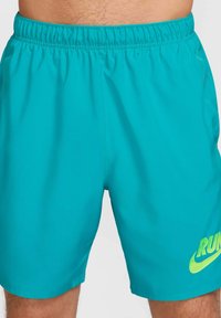 Bañador turquesa con cintura elástica, que presenta un gráfico de neón verde "RUN" y el swoosh de Nike en la parte inferior izquierda delantera.