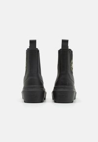 Botas de cuero negro hasta el tobillo con puntera redondeada, paneles elásticos en los laterales y una suela de goma texturizada. Presenta un parche con el logo en el talón.