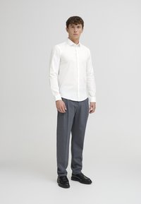 Wit overhemd met lange mouwen, gedragen met grijs gestreepte broek en zwarte dresschoenen. Eenvoudig ontwerp, gladde texturen.