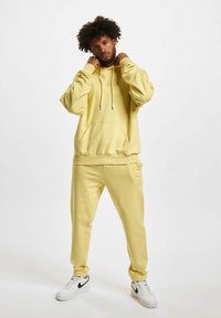 Sweat à capuche jaune avec une poche kangourou et des cordons de serrage, associé à un pantalon de jogging jaune assorti. Design simple, tissu doux et coupe décontractée.