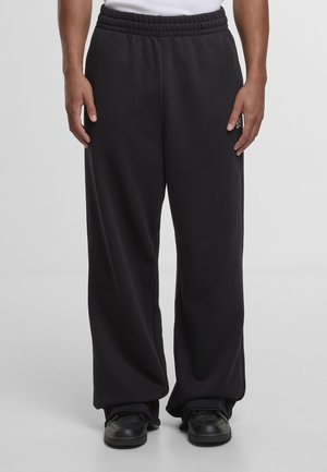 Pantalon de survêtement noir, ample, avec une taille élastique, fabriqué en tissu doux. Dispose de poches latérales et d'une coupe droite décontractée.