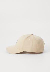 Beige baseball caps med en buet skjerm, laget av bomullstoff. Har seks ventilasjonshull og broderte detaljer på forsiden.