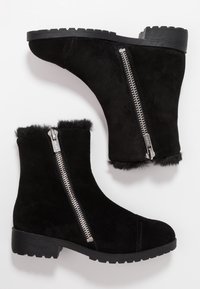 Bottines en daim noir avec fermeture éclair, ornées d'une bordure en fourrure en haut, semelle en caoutchouc et talon bloc bas. Tige texturée pour plus de détails.