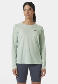 Camiseta deportiva de manga larga en un ligero tono menta con un patrón texturizado, cuello redondo y detalle de logo. Combinada con pantalones cortos ajustados en color marino.