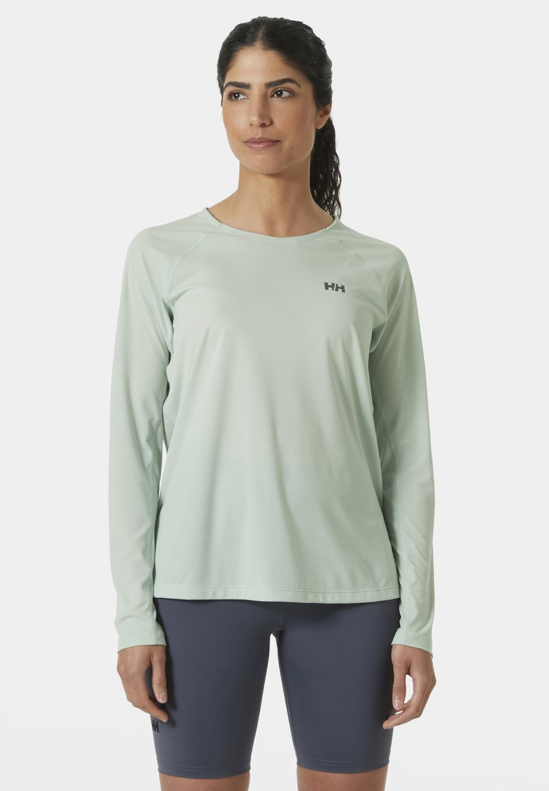 Camiseta deportiva de manga larga en un ligero tono menta con un patrón texturizado, cuello redondo y detalle de logo. Combinada con pantalones cortos ajustados en color marino.