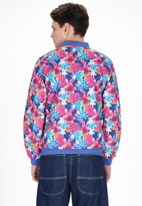Jachetă bomber florală cu un fundal vibrant bleu, flori roz și turcoaz, manșete cu riburi și guler solid bleu.