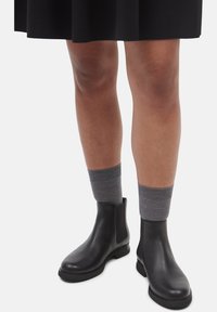 Black leather ankle boots with elastic side panels, paired with gray ribbed socks, displayed against a light background.