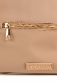 Borsa in nylon beige con zip dorata e etichetta con marchio. Texture liscia con forma rettangolare, che evidenzia il design minimalista.