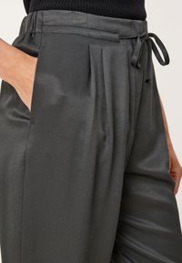 Grijze geplooide broek met een gladde textuur, een trekkoord in de taille en zijzakken. Het materiaal heeft een subtiel diagonaal patroon.