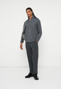 Cămașă gri cu nasturi, cu o textură subtilă, combinată cu pantaloni gri închis și pantofi negri. O geantă gri este aruncată pe umăr.