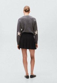 Maglione grigio lavorato a maglia con accenti a stella sulle maniche, abbinato a una gonna pieghettata nera e scarpe nere con flat. Design semplice e monocromatico.