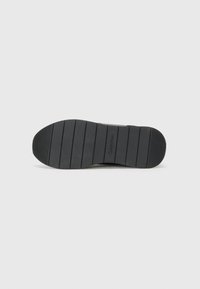Zwarte rubberen sneakerzool met een gestructureerd patroon en een ronde hak. Heeft de tekst "Calvin Klein" in reliëf aan de zijkant.