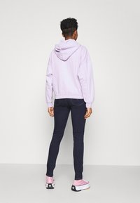 Sudadera lavanda con bolsillo canguro y capucha con cordón, combinada con jeans oscuros ajustados y zapatillas rosas con detalles de estrellas negras.