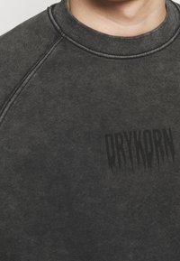 Ciemnoszara bluza z prążkowanym dekoltem typu crew, wykonana z teksturowanej tkaniny, z czarnym logo "DRYKORN". Szczegóły z kontrastującymi przeszyciami.