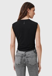 Top nero senza maniche realizzato in tessuto morbido con una silhouette aderente. Abbinato a jeans grigi sbiaditi a vita alta con cuciture in evidenza.