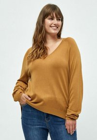 Pull en v jaune moutarde en maille douce avec des manches longues, coupe relaxe et ourlet côtelé. Porté sur un jean bleu.
