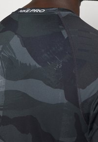 Camiseta ajustada Nike Pro en negro con un patrón de camuflaje oscuro texturizado. Presenta un cuello redondo y costuras planas para mayor comodidad.
