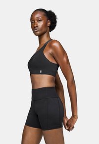 Sujetador deportivo negro con un diseño de tirante único; combinado con pantalones cortos negros de cintura alta que presentan costuras visibles y una textura suave.