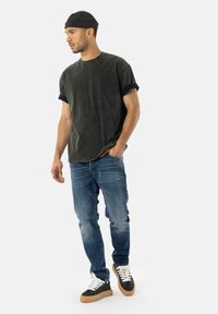 Camiseta negra de manga corta, con textura desgastada, corte relajado, combinada con jeans azules y zapatillas negras con cordones blancos y suelas beige.