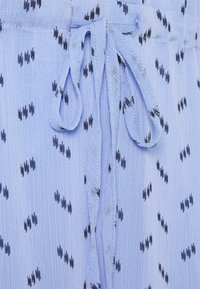 Tissu bleu clair avec un détail de nœud noué et de petits motifs abstraits noirs dispersés, montrant la texture et les points de couture.