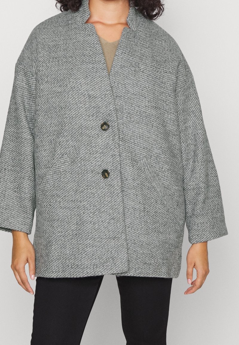 Cappotto grigio con texture, dal taglio ampio, caratterizzato da colletto a revers, due tasche frontali e due bottoni per la chiusura.