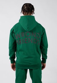 Zelená mikina s kapucí se černým nápisem "WRONG FRIENDS" na zadní straně. Obsahuje stahovací kapuci, žebrované manžety a volný střih.