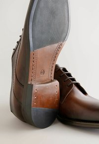 Brown leather dress shoes with a contrasting brown and black rubber sole. Features include laces and stitching details along the sides. Size 42.