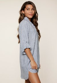 Camisa de botones a rayas en azul claro y blanco, con mangas enrollables, un bolsillo en la parte delantera y un corte relajado con dobladillo curvo.