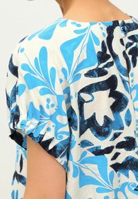 Blusa de terciopelo azul y blanca con un estampado, con mangas cortas y recogidas; corte holgado, tela texturizada; cuenta con un pequeño cierre de botón en la parte posterior.